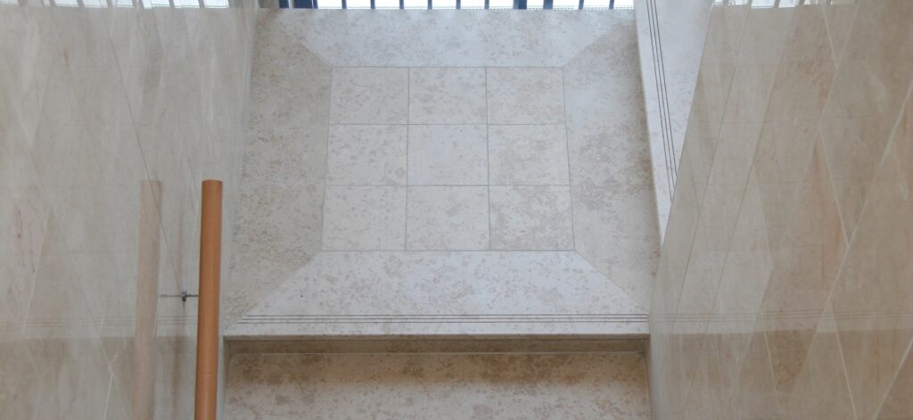 Szimmetrikus raszter egy világos mészkővel burkolt lépcsőház pihenőjén • Symmetrical grid on the landing of a staircase paved with light limestone